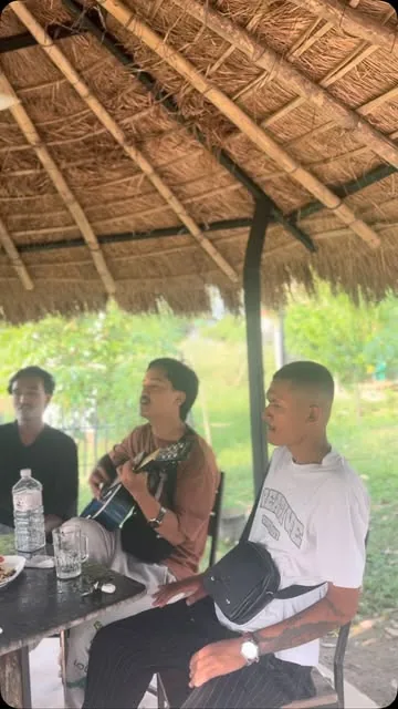 Musicians playing acoustic guitar under a thatched hut.