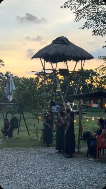 Guests gathered under the raised thatched machan as the sun sets over the field.